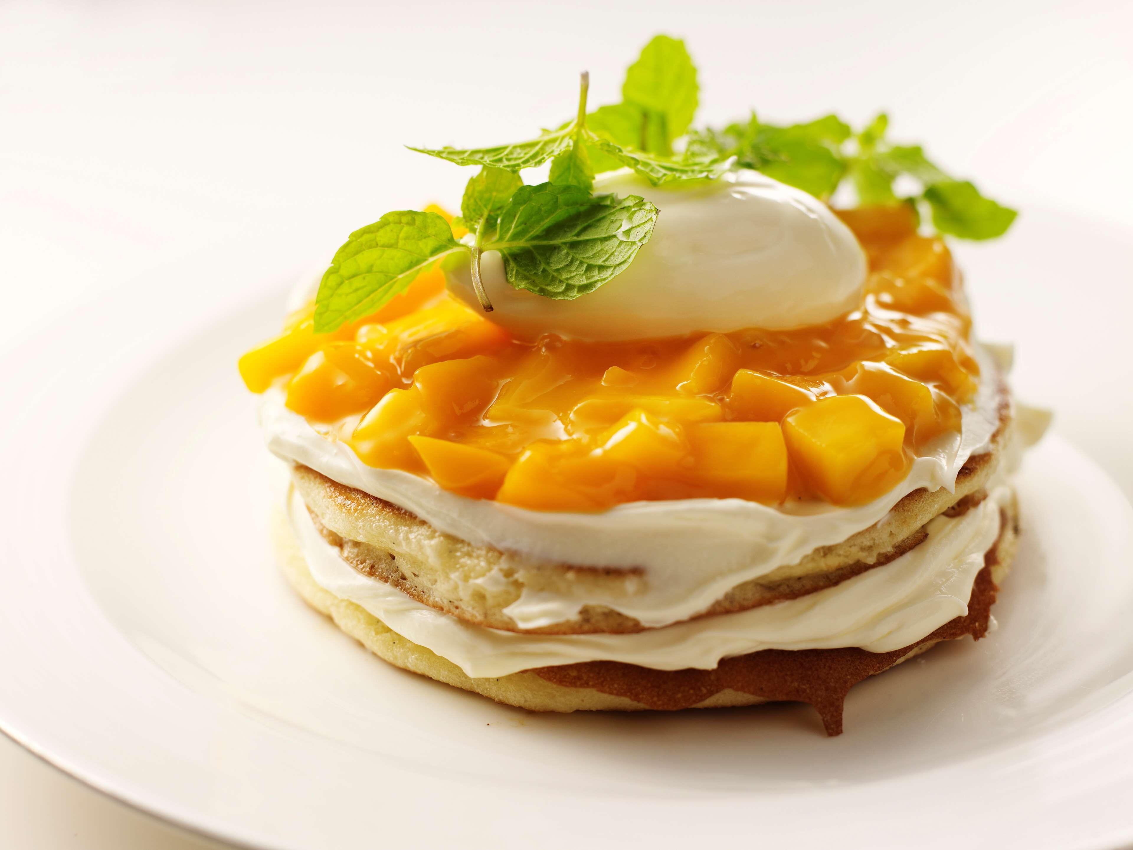 A dessert with mango chunks and whipped cream on a cake.