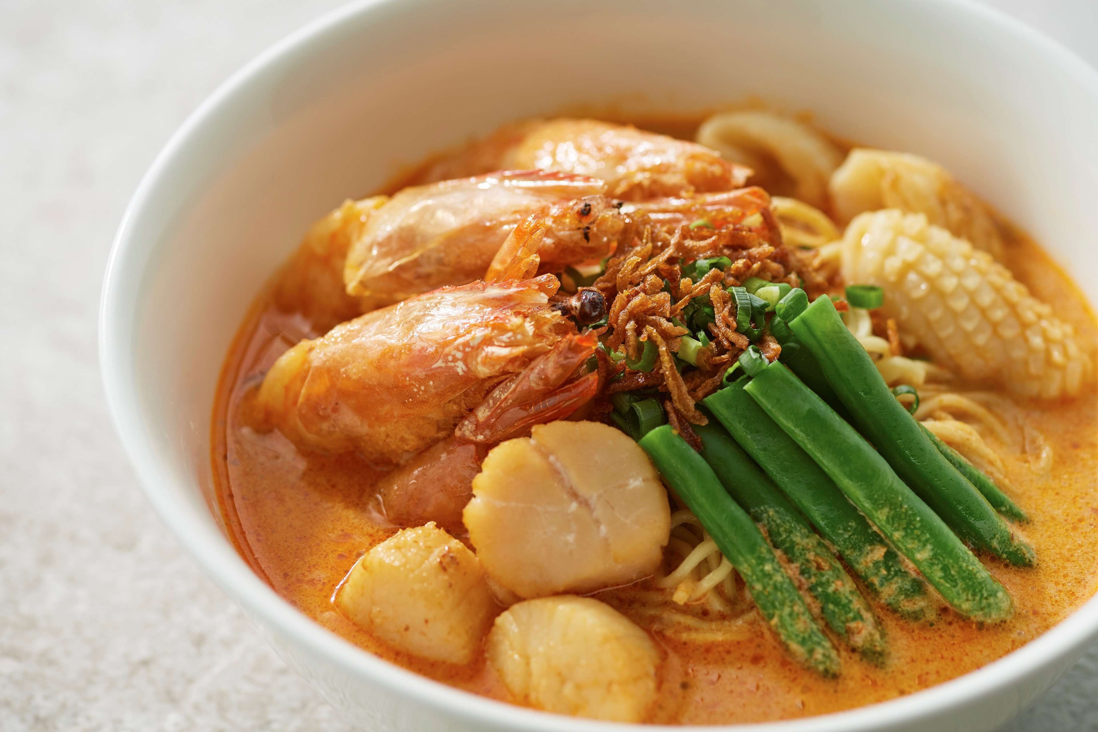 A bowl of soup with various ingredients like shrimp, corn, and green onions.