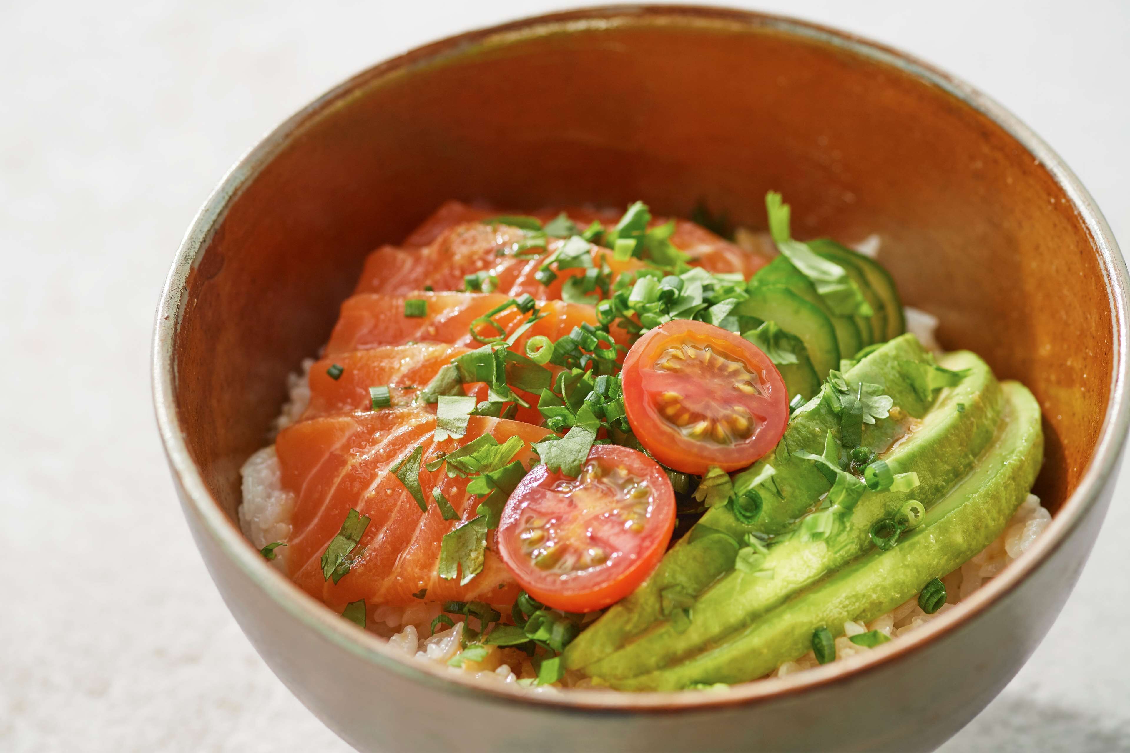 Un plato de comida con salmón, aguacate y tomates.