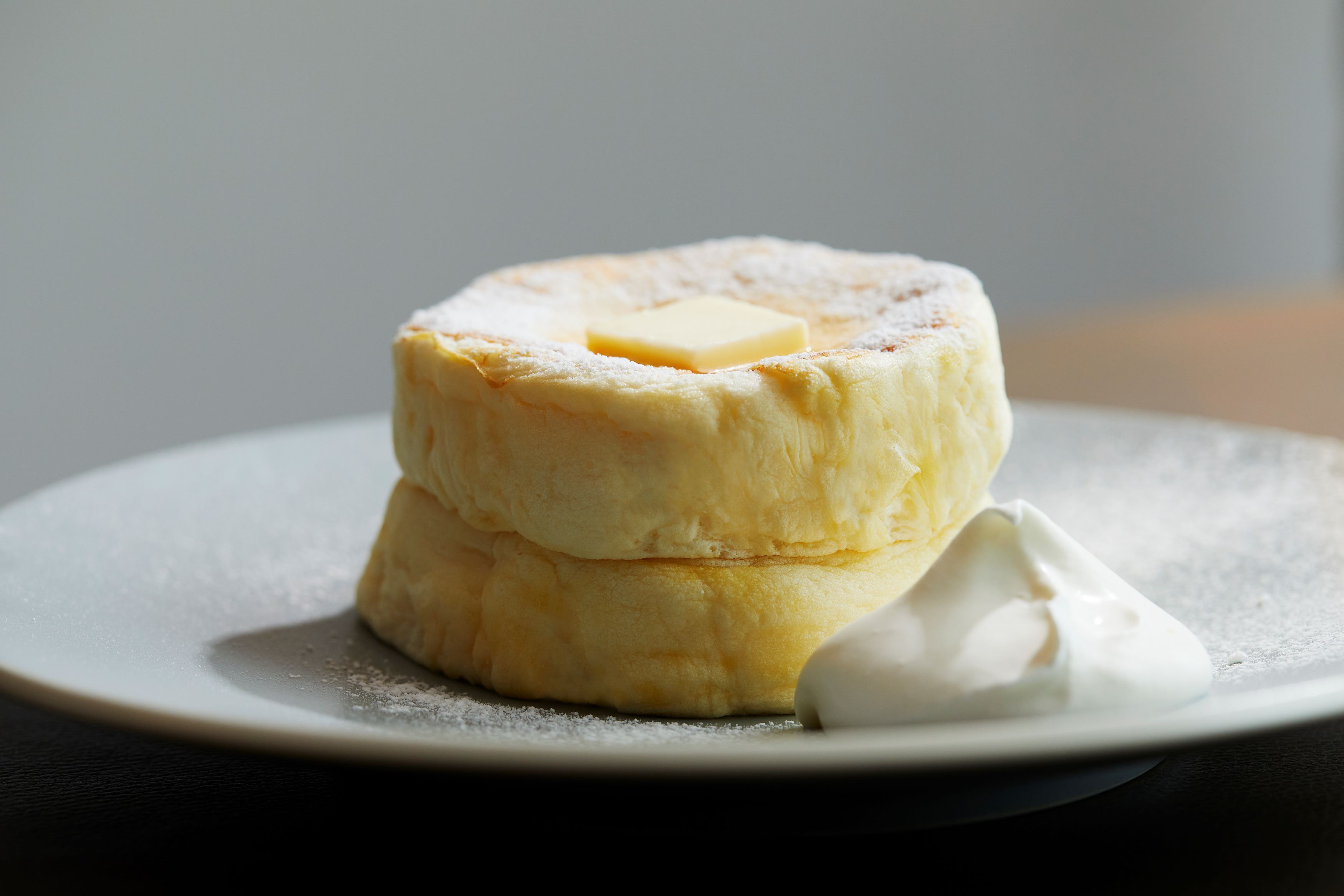 A stack of pancakes with a pat of butter and a dollop of whipped cream on a plate.
