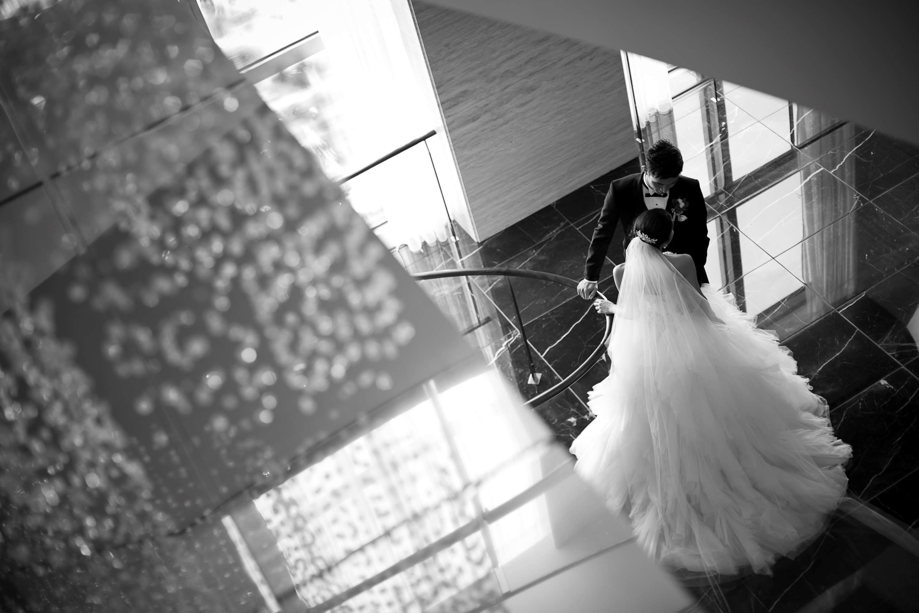 A person in a wedding dress descending a staircase in a modern building with reflective glass and marble floors.