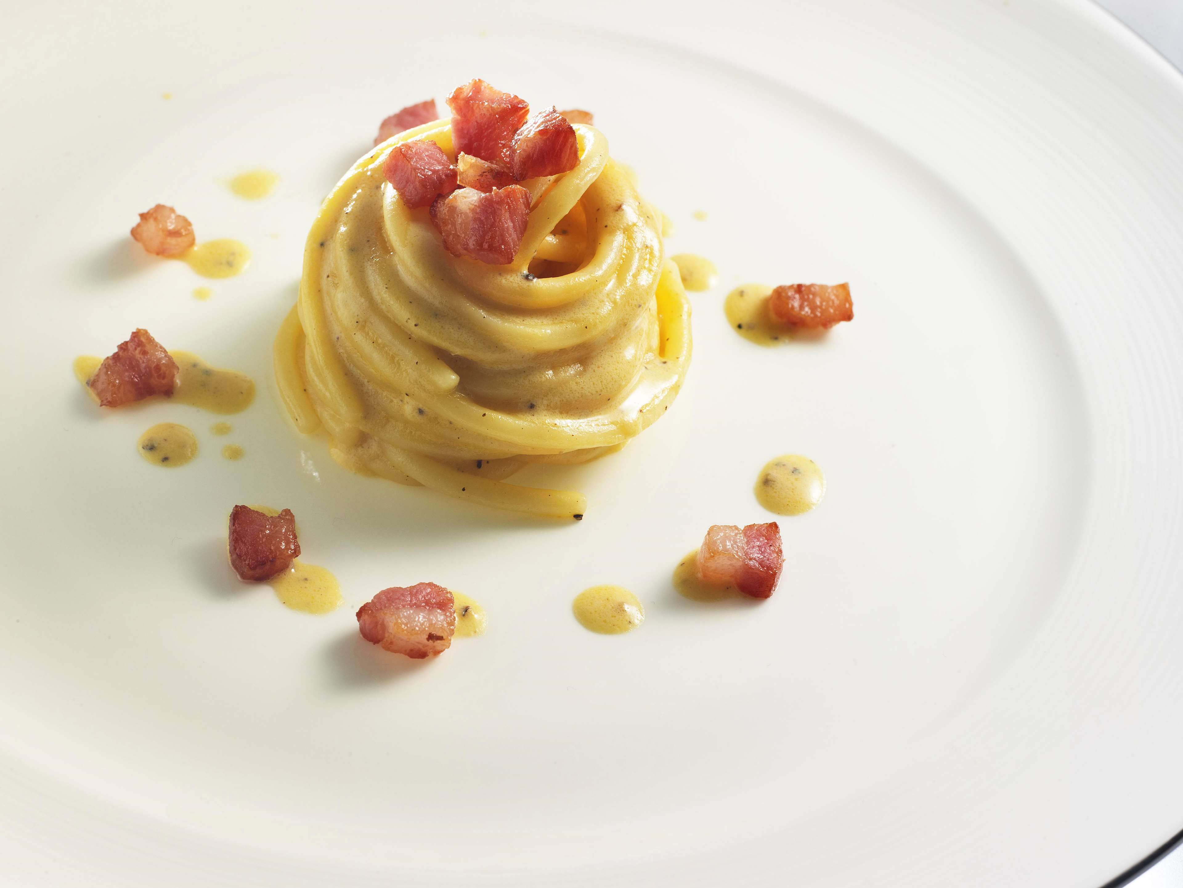 A plate of pasta with a creamy sauce and garnished with bacon bits.