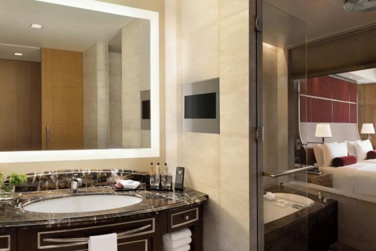 A modern bathroom with a large mirror, a marble sink, and a separate vanity with a mirror. There is a shower area visible in the background.