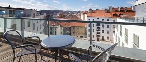 A balcony with a table and chairs, offering a view of buildings and a clear sky.