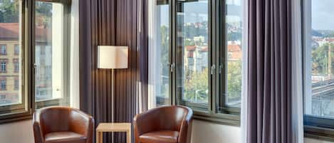 A modern hotel room with large windows, two leather armchairs, a small table, and a lamp.