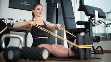 Een persoon die oefeningen doet met weerstandsbanden in een sportschool met fitnessapparatuur en gewichten.