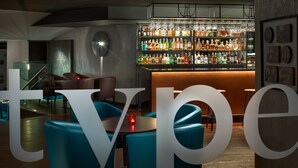 A modern bar area with a variety of liquor bottles and glasses on shelves. There are blue chairs and a wooden table in the foreground. - Hermitage Hotel Prague (Prague)
