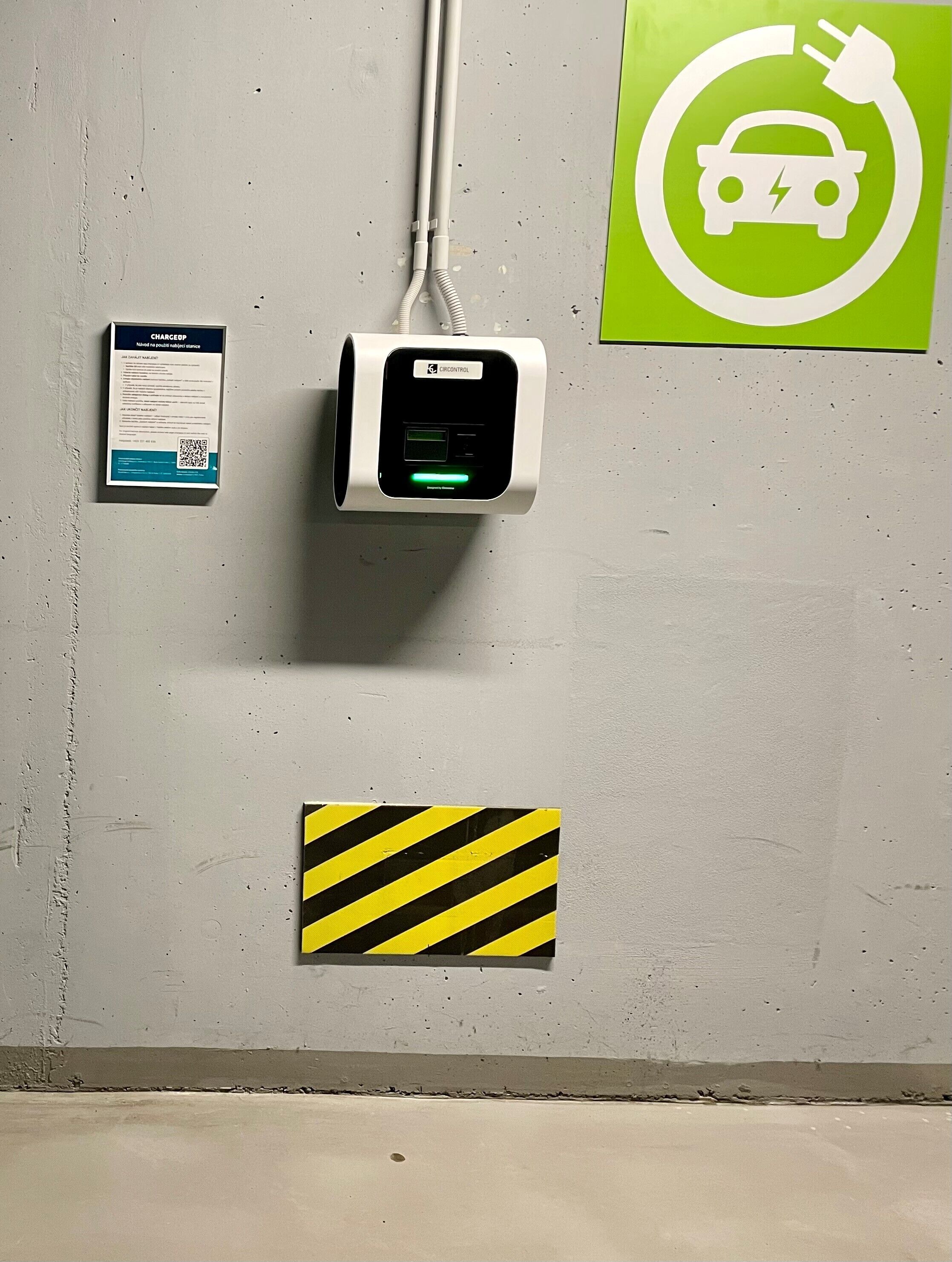 A wall-mounted charging station with a green indicator light, a QR code, and a caution sign.
