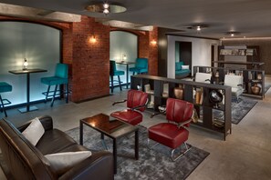 A modern lounge area with leather sofas, teal chairs, and a brick wall.