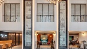 A modern hotel lobby with a central seating area, a bar, and informational posters on the walls. - Hermitage Hotel Prague (Prague)