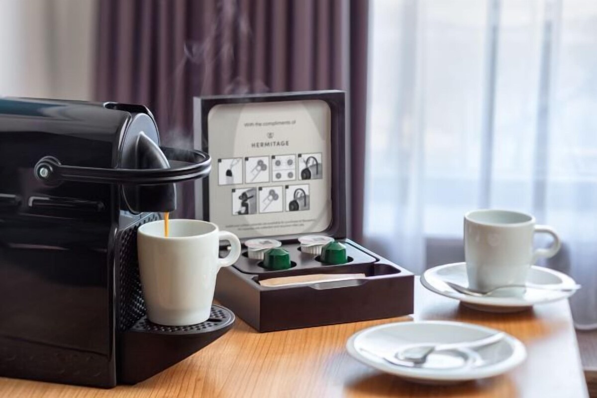 A coffee maker with a manual, two white cups, and a tray with a plate and a cup.