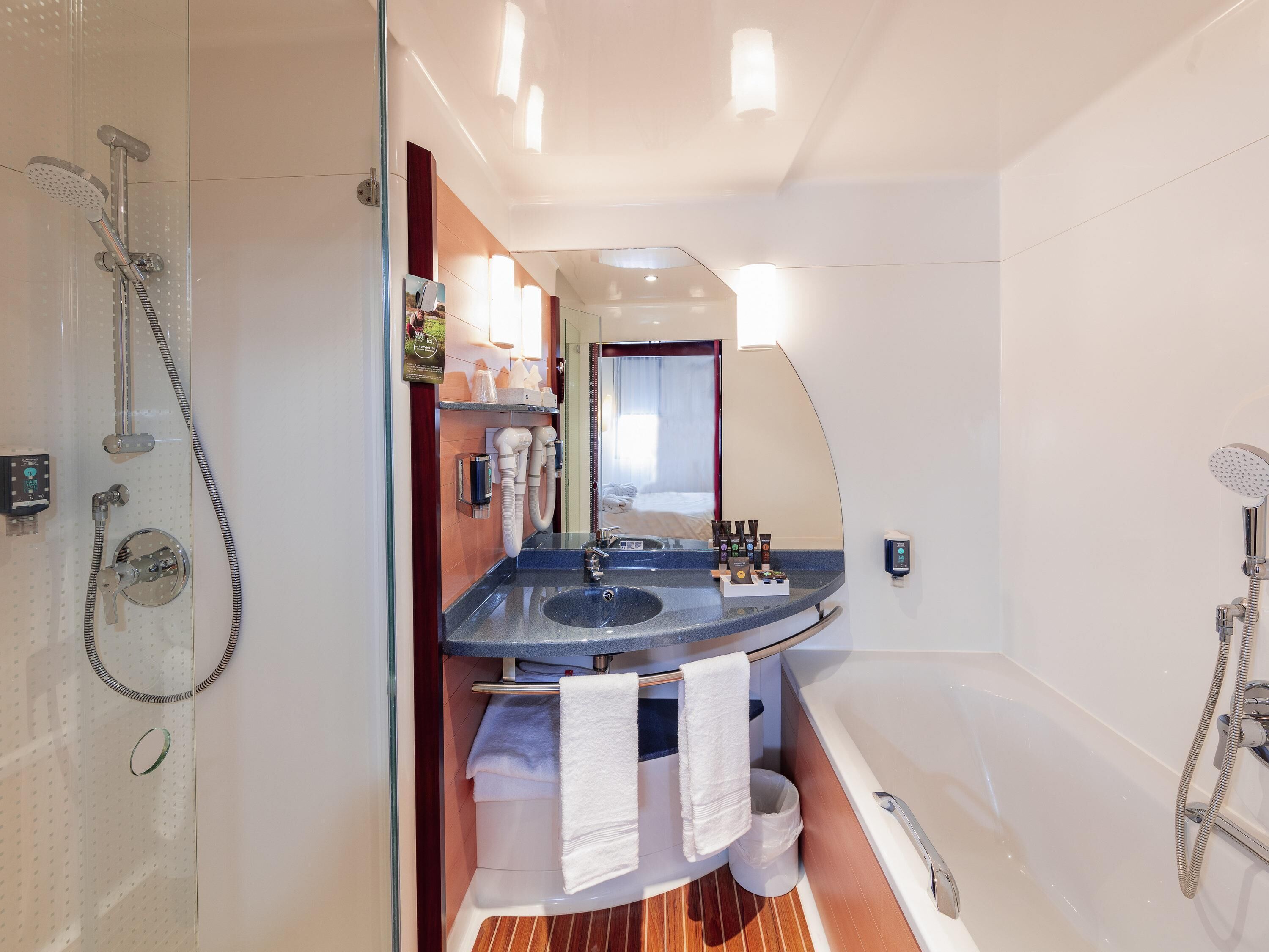 A modern bathroom with a glass shower enclosure, a built-in sink, a bathtub, and a vanity with a mirror.