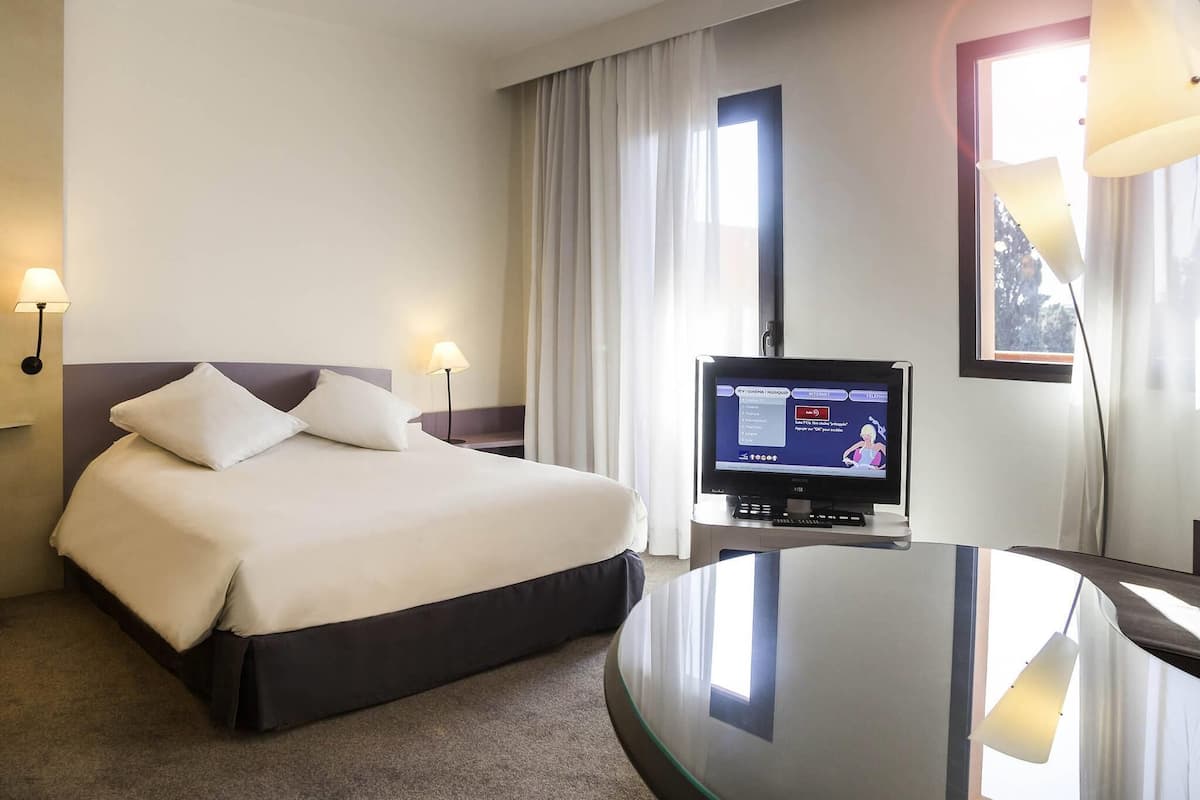 Una habitación de hotel con una cama, televisión y escritorio.