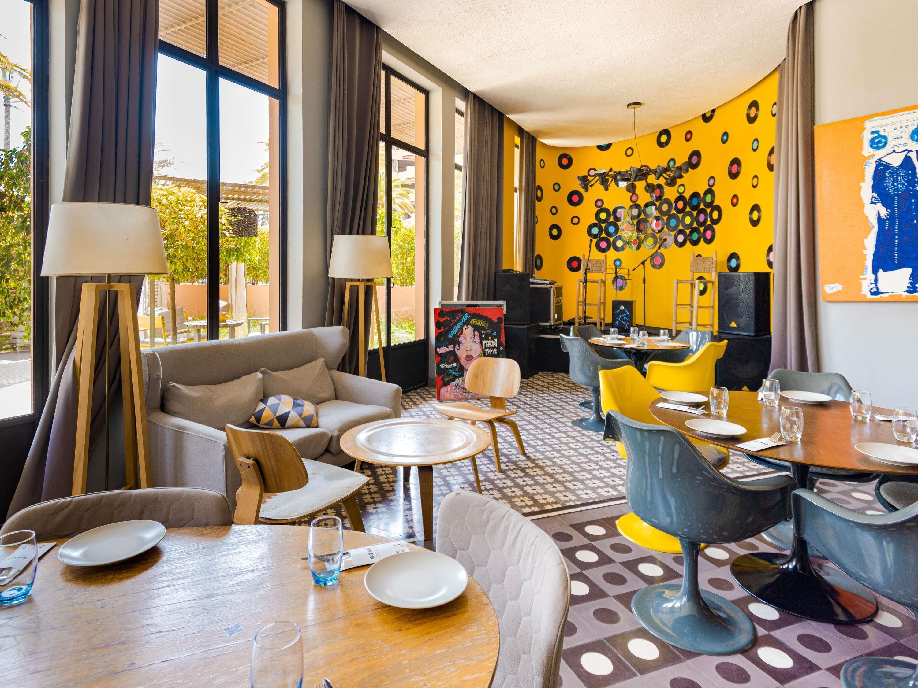 A hotel room with a sofa, dining table, chairs, and a wall decorated with vinyl records.