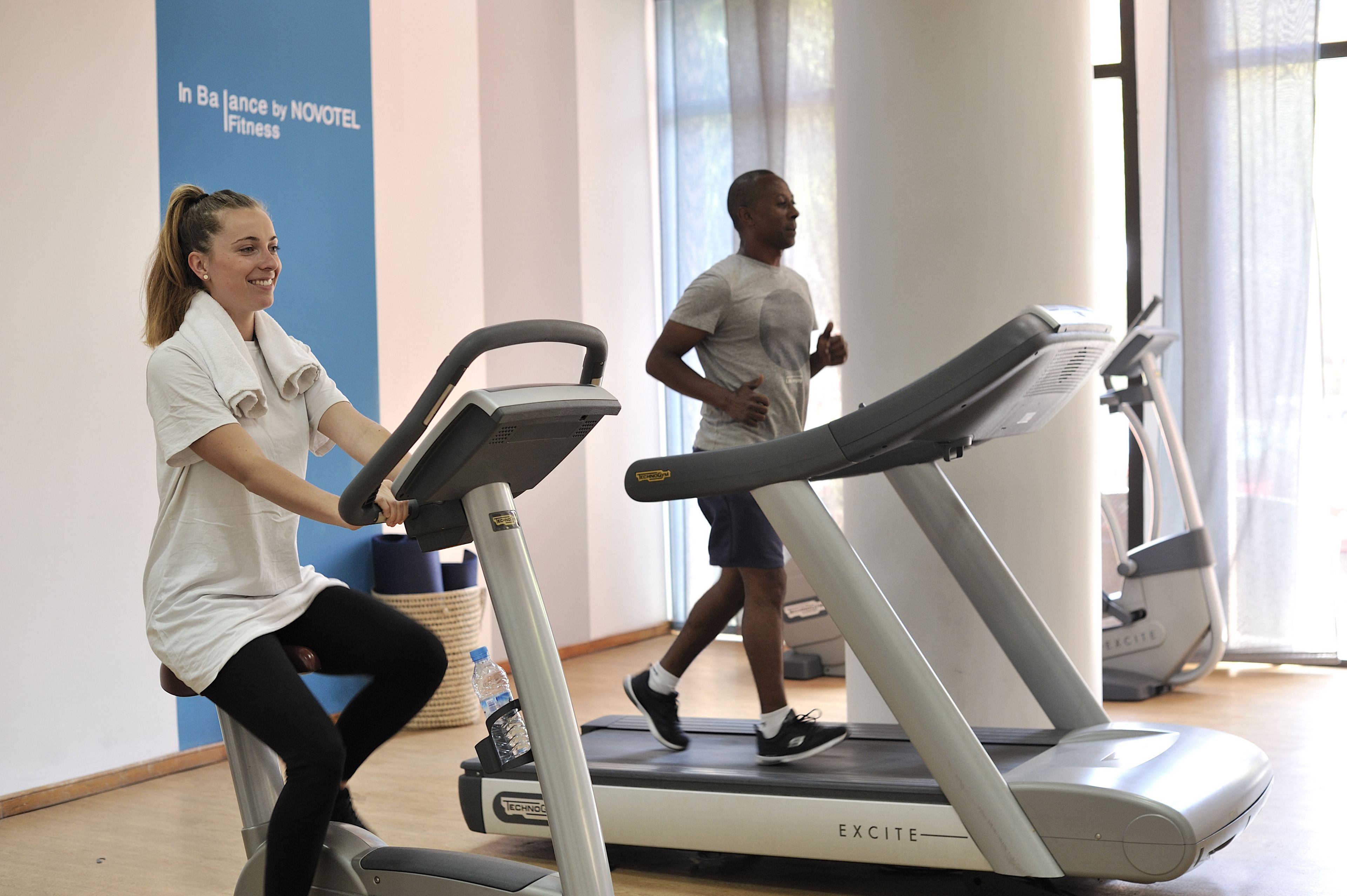 A fitness center with treadmills and a wall sign reading "In Balance by NOVOTEL Fitness".
