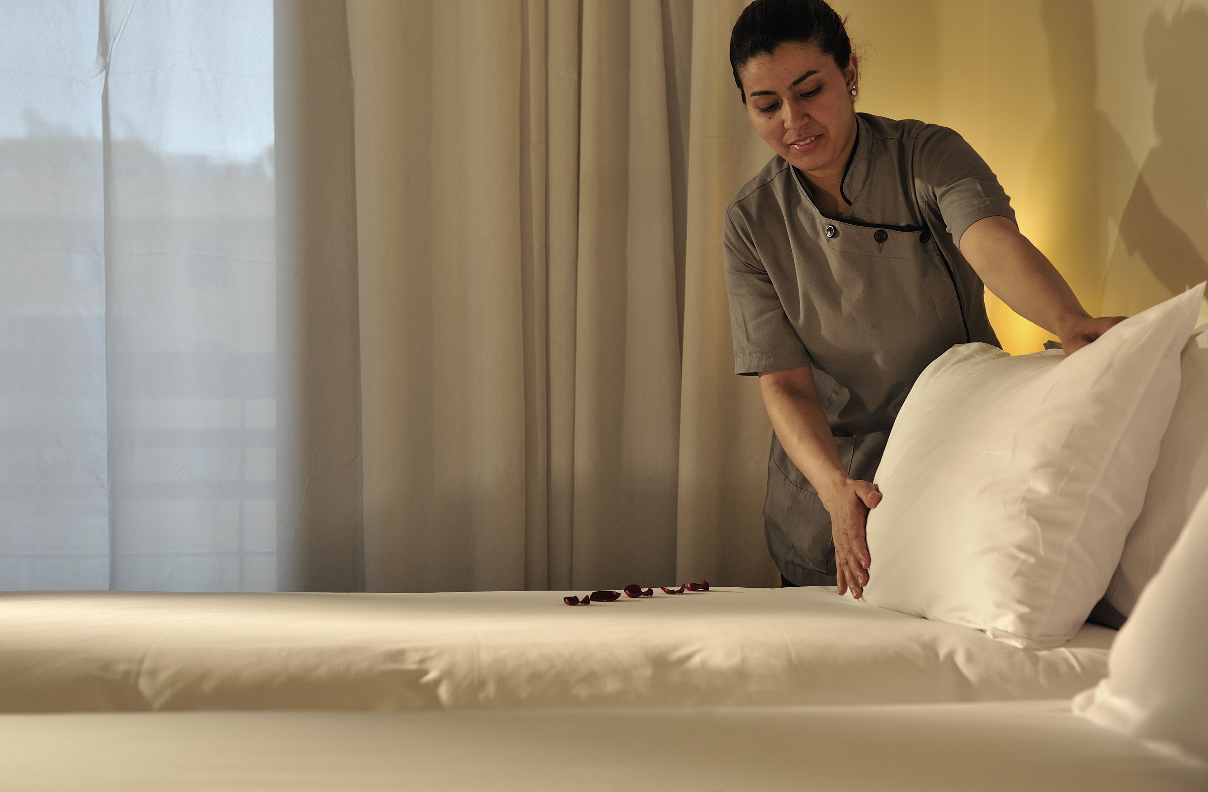A person adjusting a bed in a room with a window and curtains.