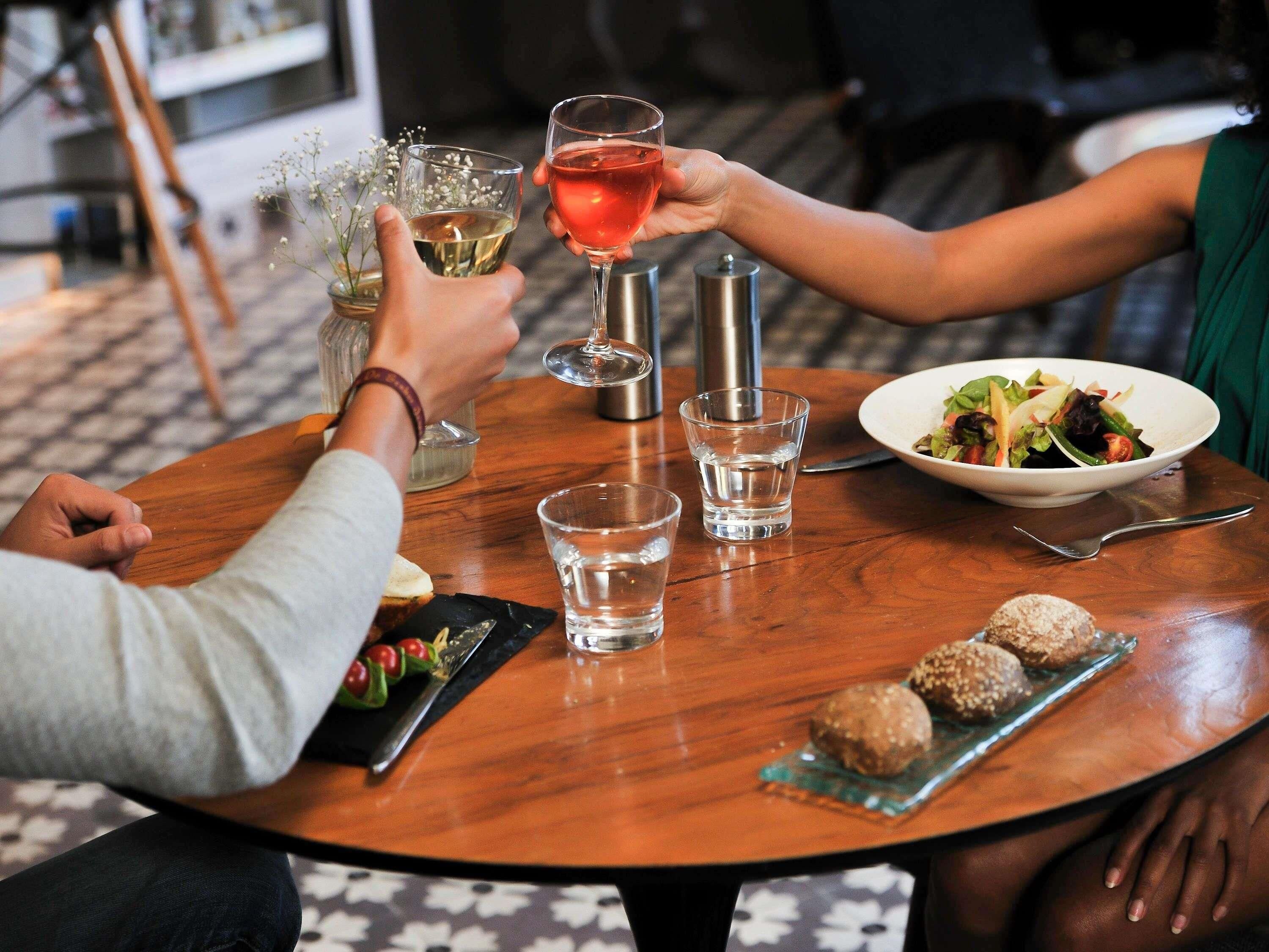 Een ronde houten tafel met een salade, twee glazen wijn en een schaal noten.