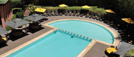 A pool area with lounge chairs and umbrellas, surrounded by greenery.