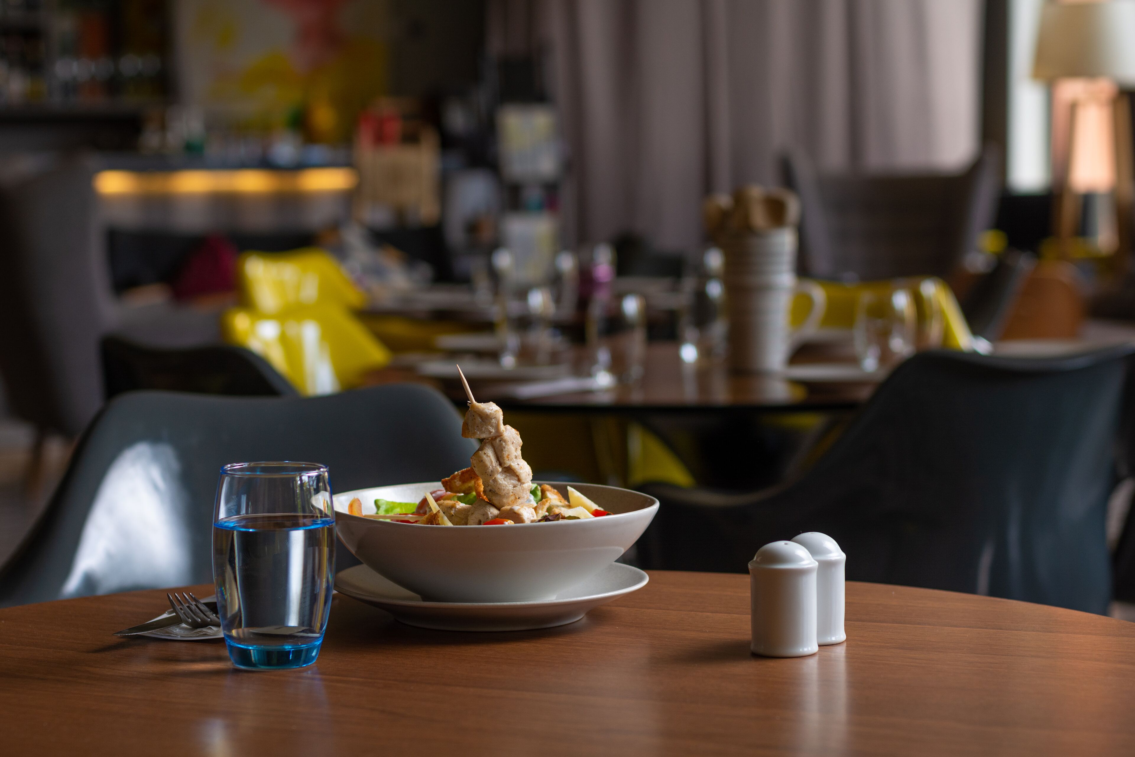 Una mesa de comedor con un plato de comida, un vaso de agua y saleros y pimenteros.
