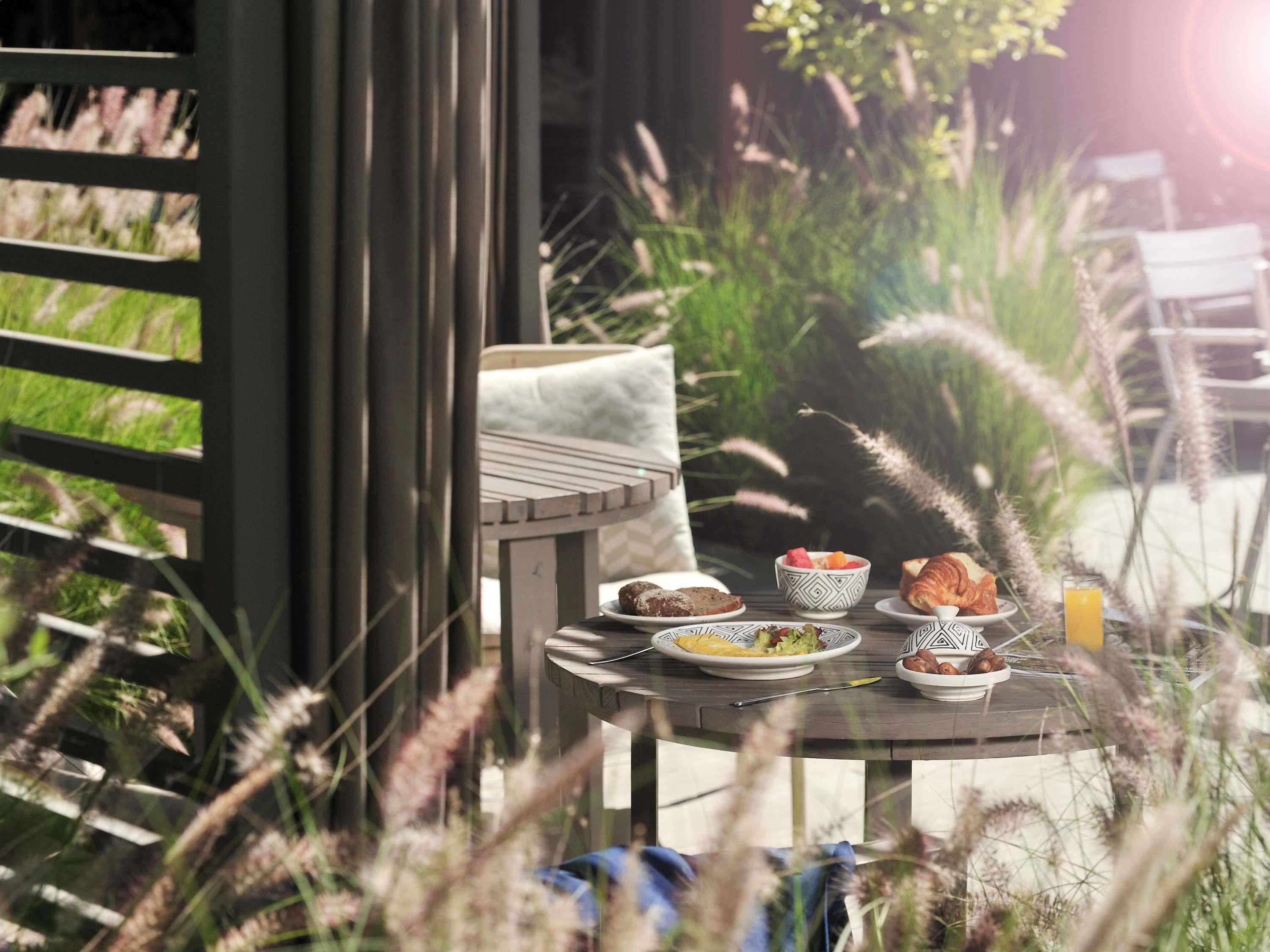 A round table with plates of food, a chair, and a window overlooking greenery.
