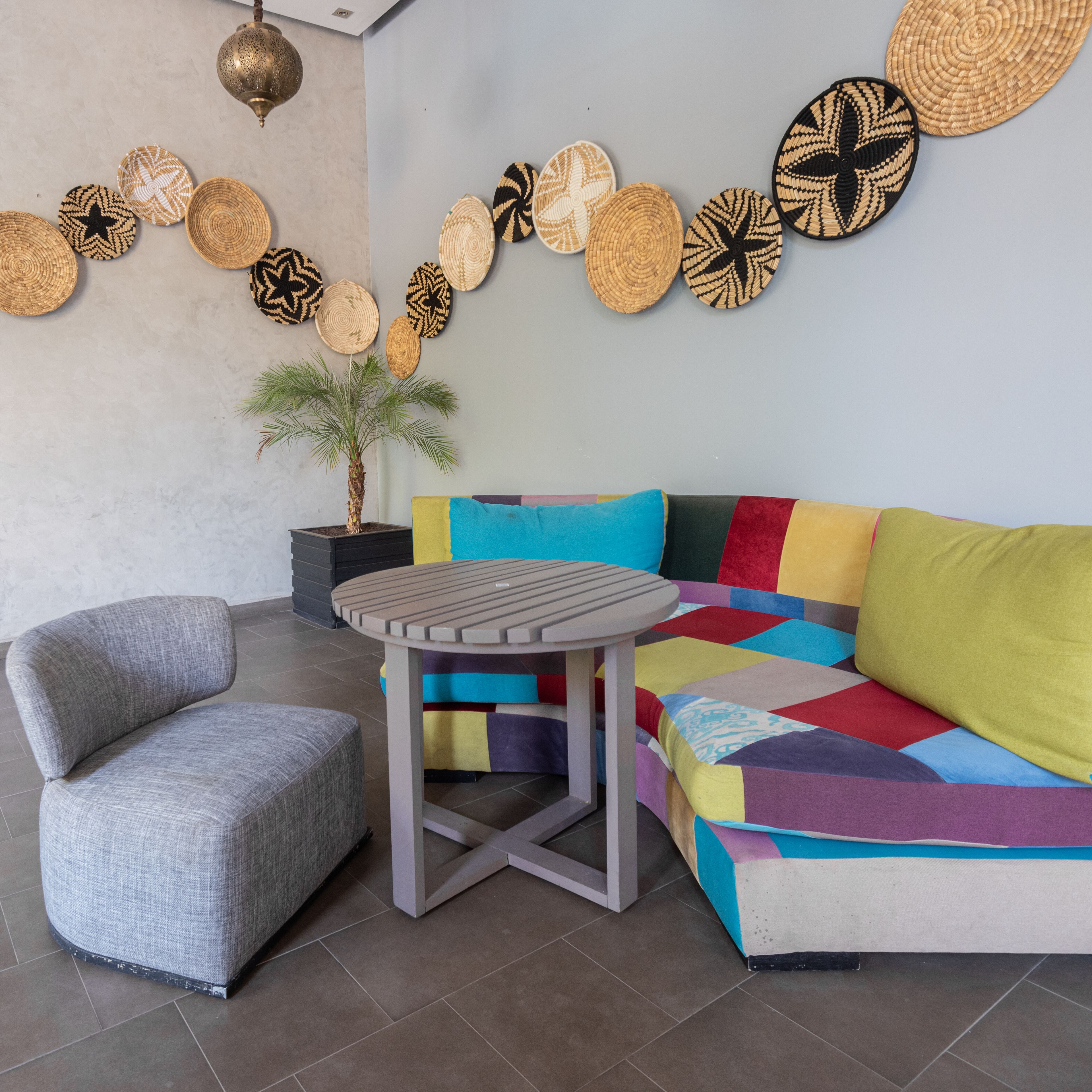 En moderne stue med en grå lænestol, et lille rundt bord, en farverig sofa og en potteplante.
