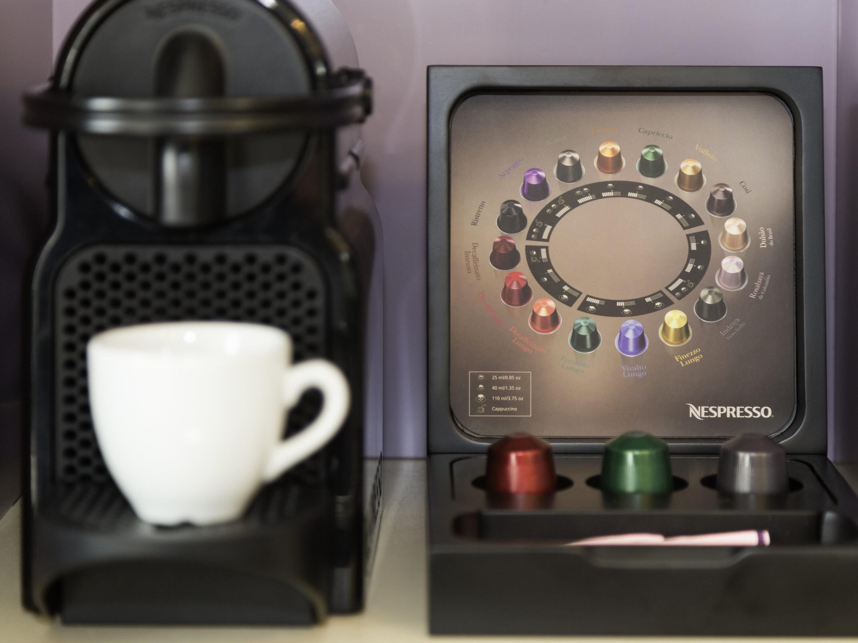 Una máquina de café Nespresso con un portacapsulas y una taza blanca.