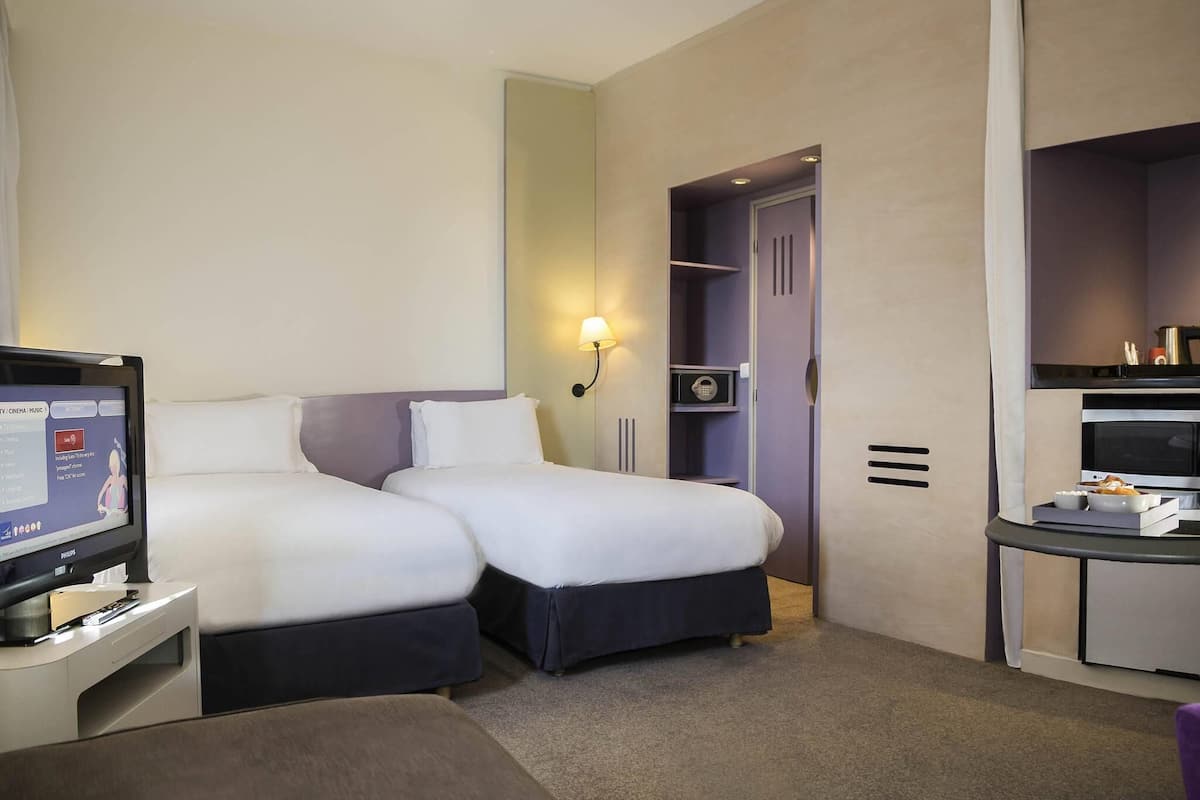 Una habitación de hotel con dos camas, un escritorio con computadora, televisión y minibar.