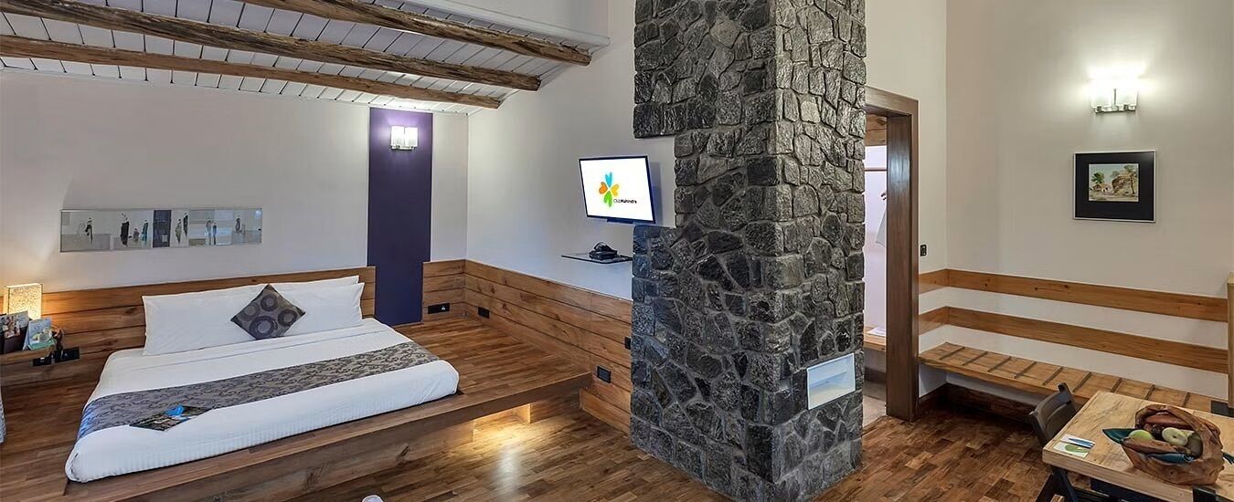 Ein Schlafzimmer mit einem Bett, einer Steinsäule, einem Schreibtisch mit Computer und einer Bank.