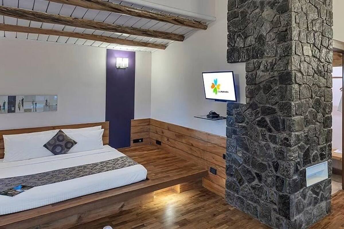 A bedroom with a bed, a stone pillar, a desk with a computer, and a bench.
