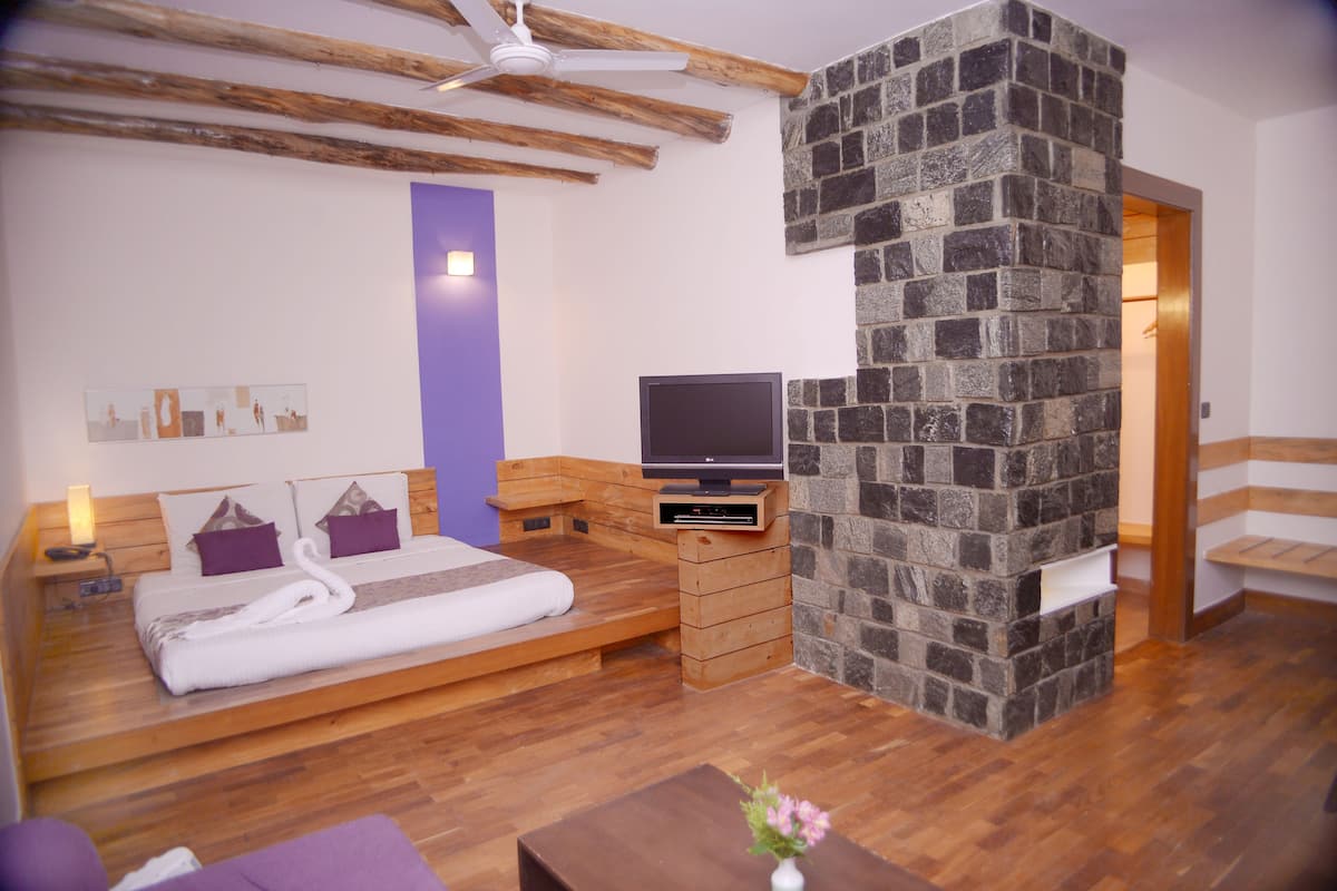 A modern bedroom with a stone fireplace, wooden furniture, a flat-screen TV, and a bed with a swan-shaped pillow.
