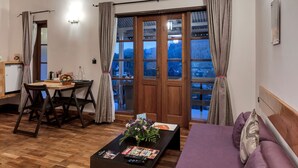Una sala de estar moderna con piso de madera, un sofá púrpura, una mesa de centro de madera, un ventilador de techo y vistas a través de una puerta de cristal.