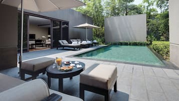 Zona de piscina exterior moderna con sillones reclinables, una mesa con desayuno y un paraguas grande.
