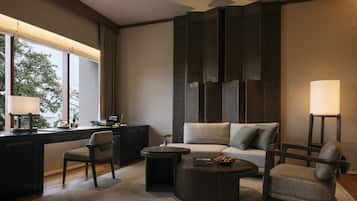 Una habitación de hotel moderna con un sofá, dos sillones, una mesita de centro, un escritorio y una lámpara.