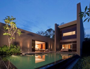 Un edificio moderno con piscina, asientos exteriores y un interior bien iluminado.