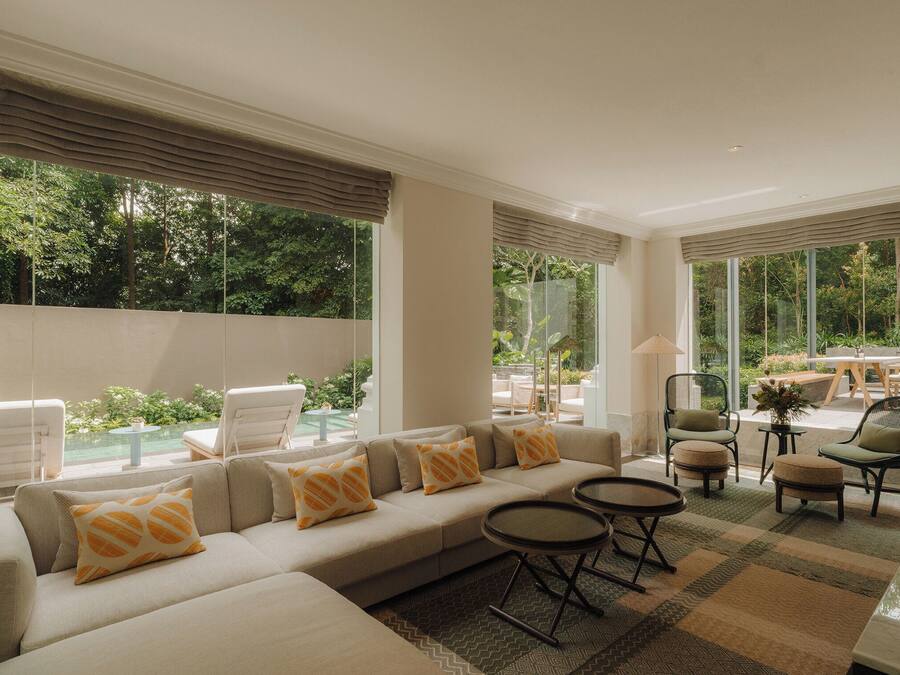 A modern living room with a beige sofa, patterned cushions, and a view of a garden through large windows.