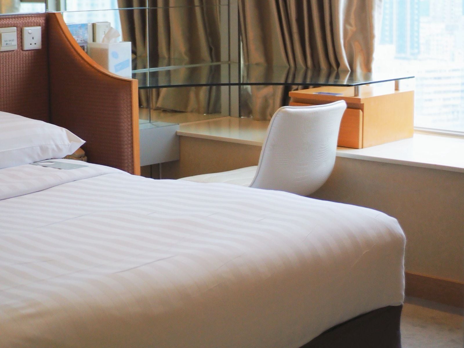 Camera d'albergo con un letto, una scrivania, una sedia, una finestra con tende e vista sulla città.