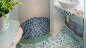 Un baño con ducha, lavamanos y una planta en maceta.