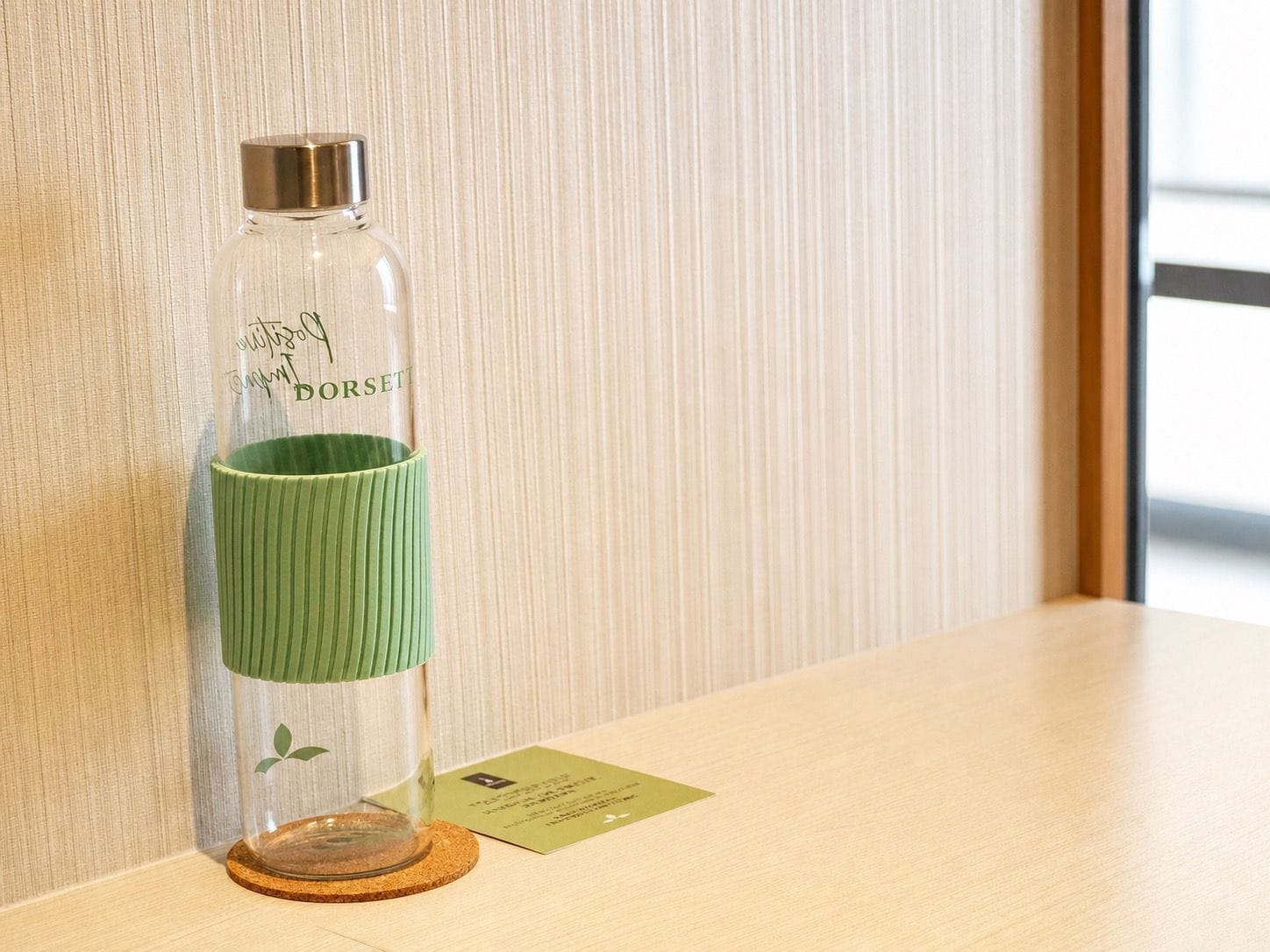 A clear glass bottle with a green label on a wooden surface, next to a small card.