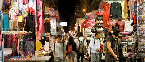 A crowded street market with various stalls selling clothes and accessories.