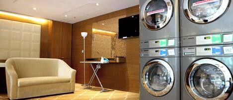 A hotel room with a sofa, a washing machine, a television, and a patterned carpet.