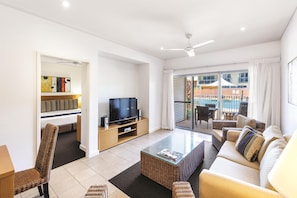 A modern living room with a flat-screen TV, a sofa, a coffee table, and a bookshelf. - Oaks Broome Hotel (Broome)