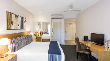A hotel room with a bed, a desk with a TV, a chair, and a ceiling fan.