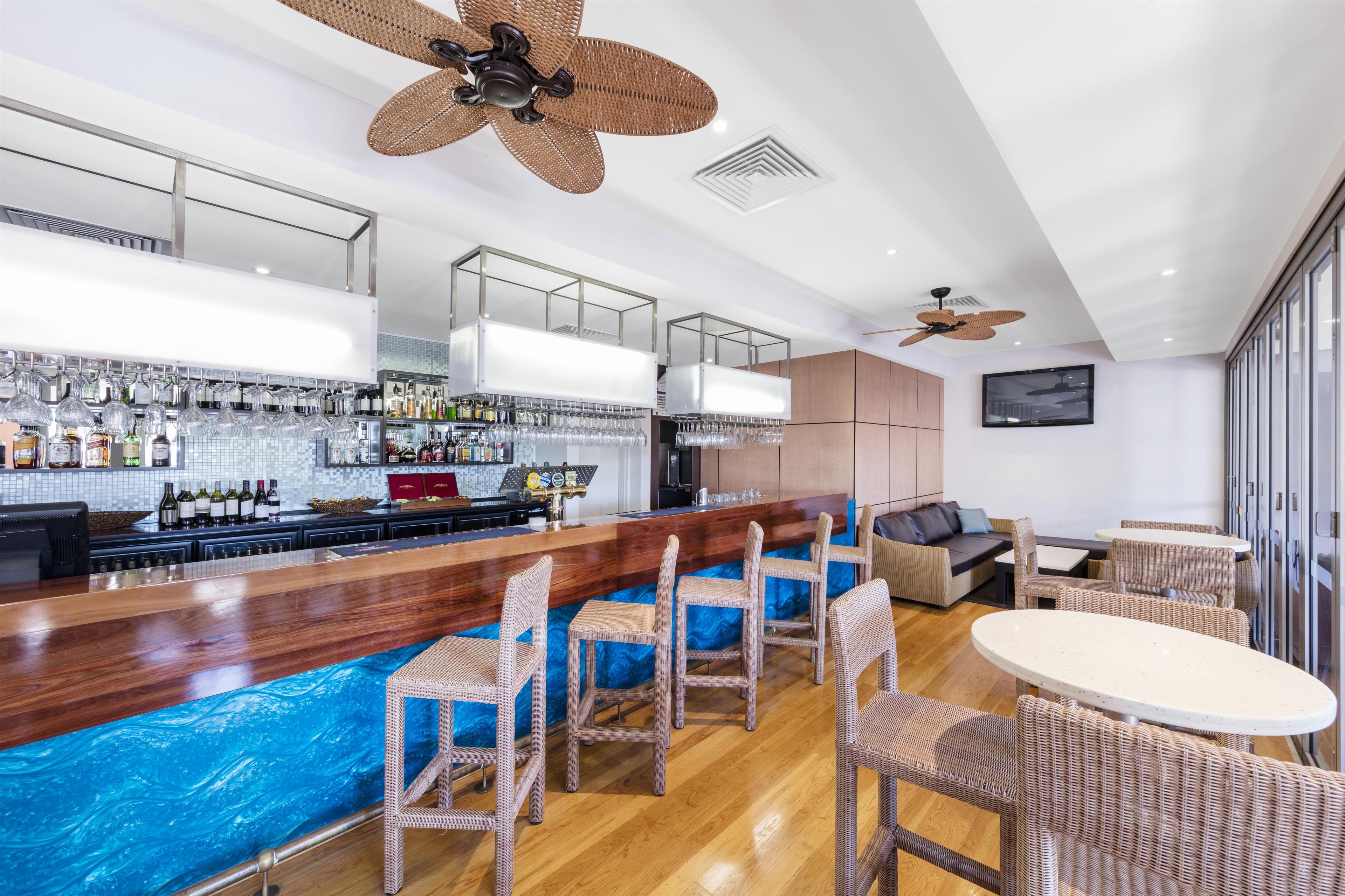 A modern bar area with a wooden counter, wicker chairs, and a large TV mounted on the wall.