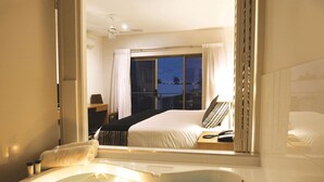 A hotel room with a large window, a bed, a bedside table, and a bathtub. - Oaks Broome Hotel (Broome)