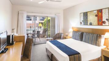 A hotel room with a bed, a desk with a television, a chair, a ceiling fan, and a view of the outside.