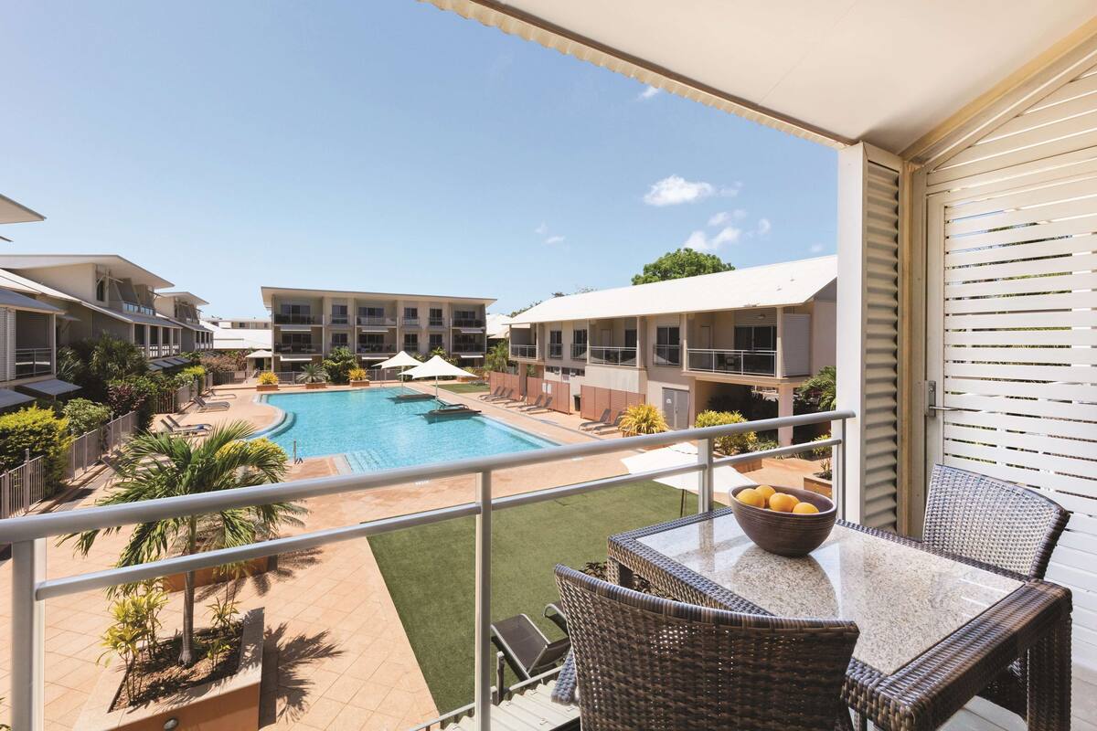 A balcony with wicker furniture overlooking a swimming pool and adjacent buildings.