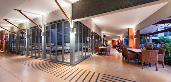 A modern indoor space with glass partitions, tables, chairs, and a mix of natural and artificial lighting. - Oaks Broome Hotel (Broome)