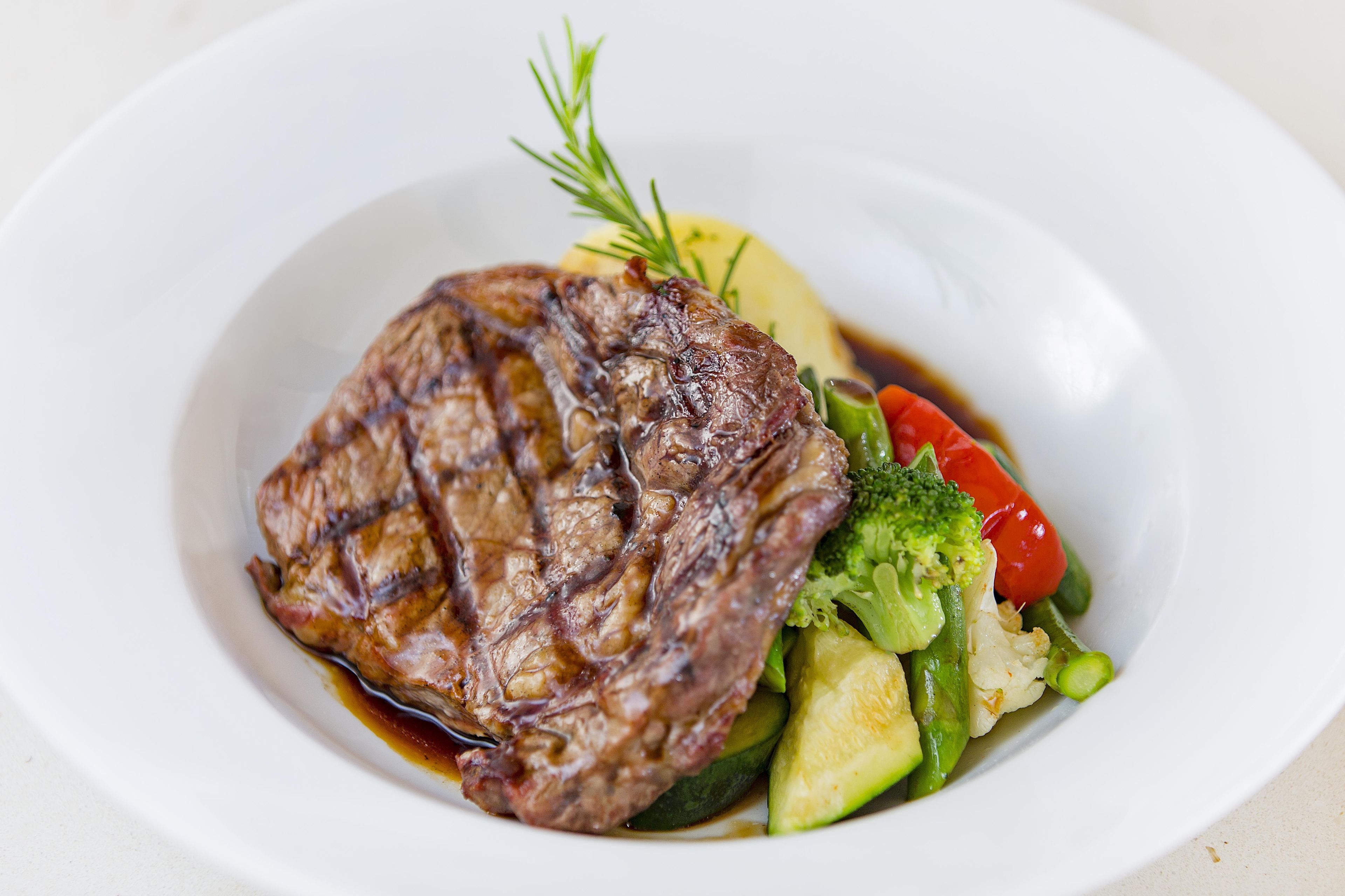 Une assiette contenant un steak, des légumes et une branche de romarin.