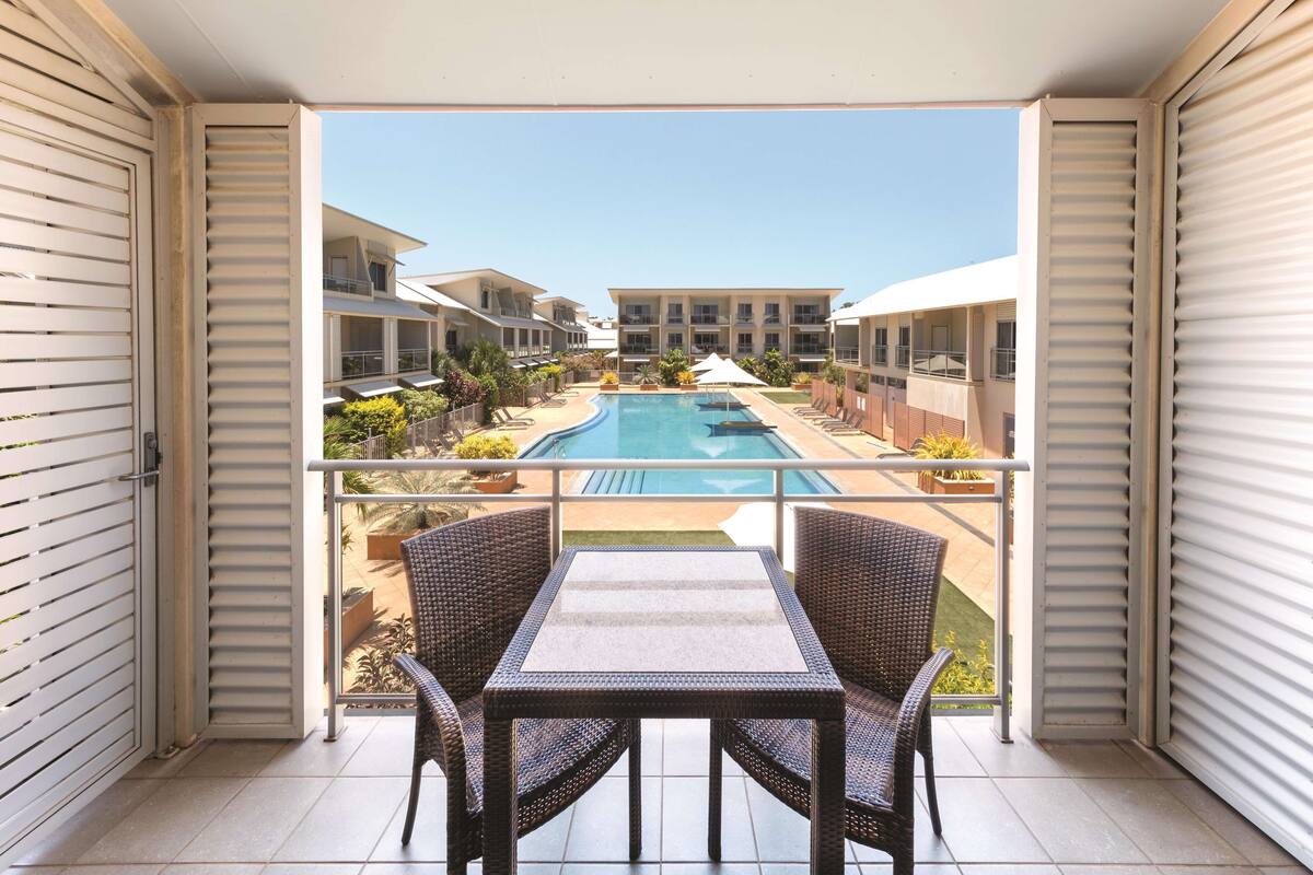 A balcony with a view of a swimming pool, wicker furniture, and a tiled floor.