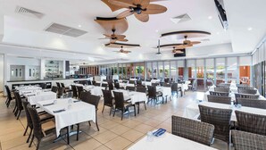 A spacious indoor dining area with multiple tables and chairs, ceiling fans, and large windows providing natural light. - Oaks Broome Hotel (Broome)